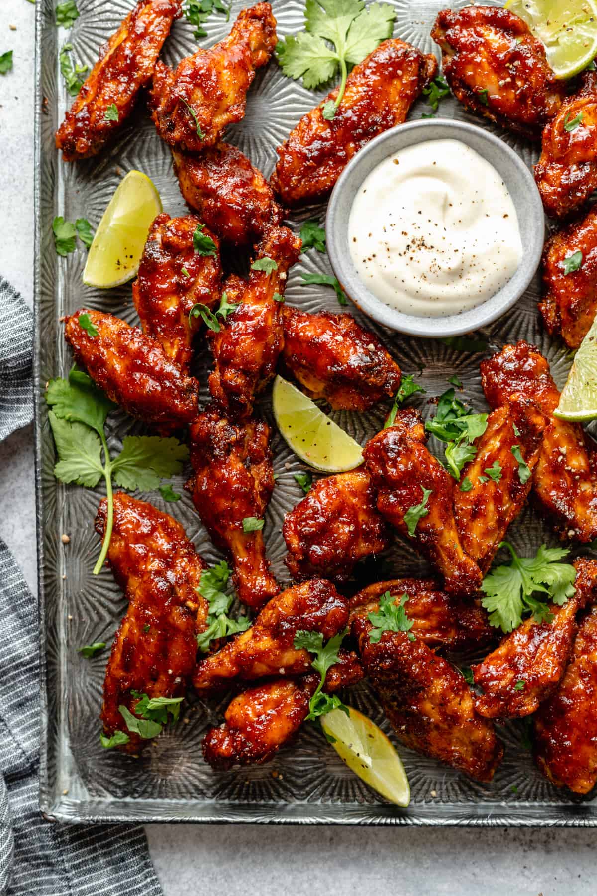 A metal tray with an array of sticky spicy chipotle lime baked chicken wings with a creamy dipping sauce.