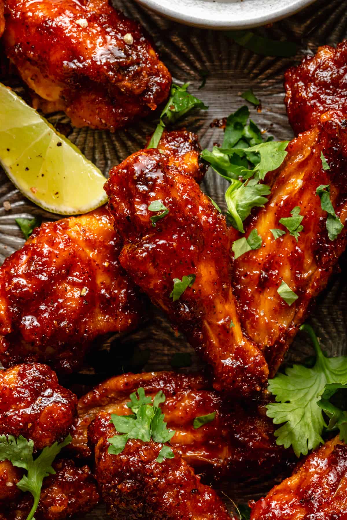 Macro of sticky crispy baked chicken wing on a metal tray with a lime wedge and coriander leaves.