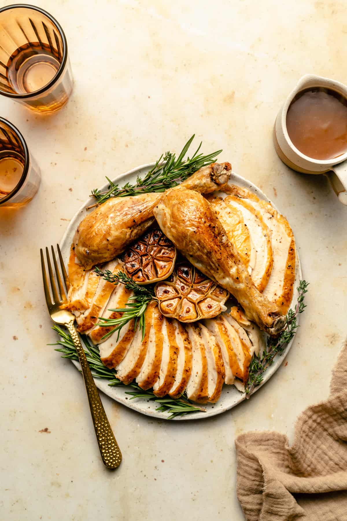 Perfect whole roasted chicken carved and served on a platter with roasted garlic and herbs and gravy and a fork to the side.