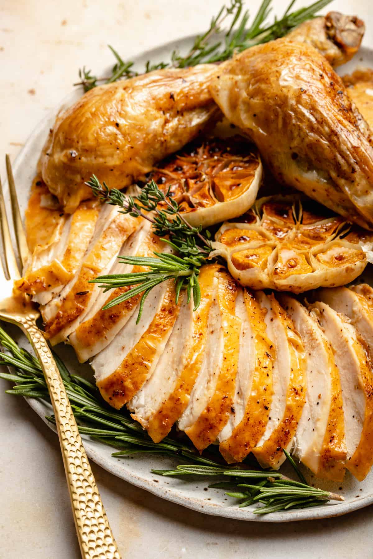 A platter showing the carved slices of chicken and two drumsticks with roasted garlic, rosemary and a fork.