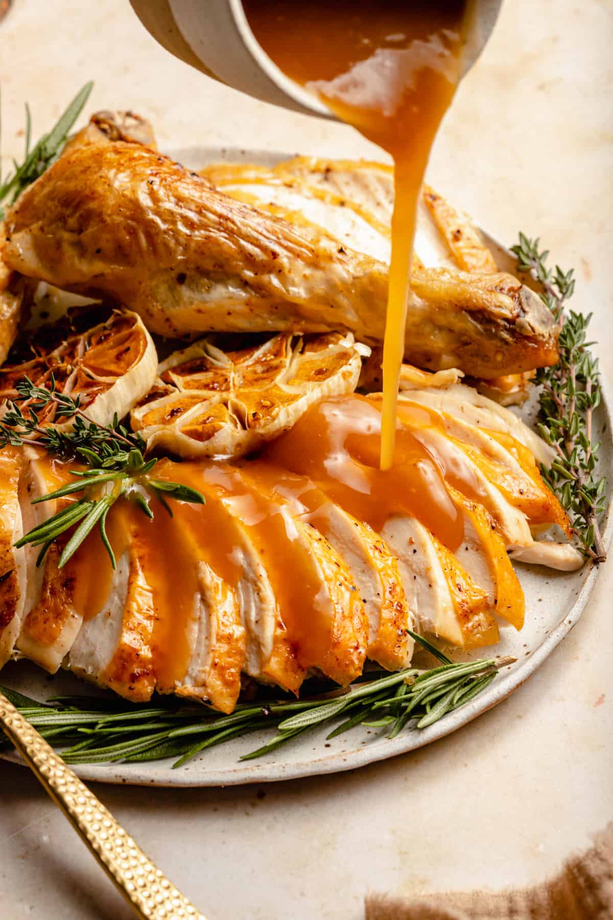 Gravy being poured over the roasted chicken on a plate with herbs. 