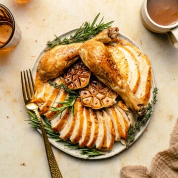 The perfect crispy whole roasted chicken carved and served on a platter with roasted garlic and rosemary with gravy and a fork.