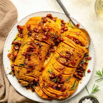 hasselback butternut squash with bacon on top served on a platter with a spoon.