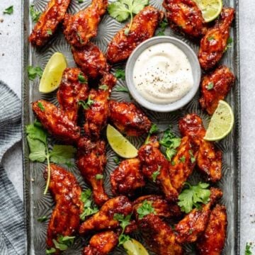 Sticky Spicy Baked Chicken Wings on a baking sheet with lime wedges and dipping sauce.