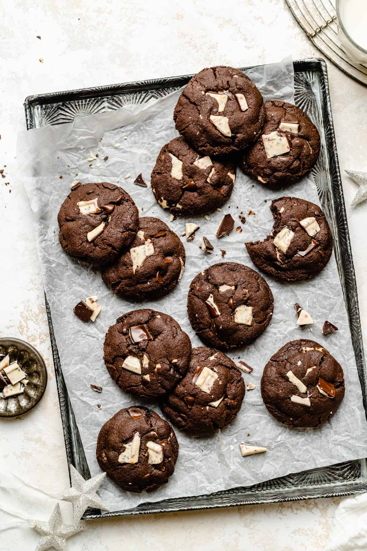 An array of mint chocolate chip cookies on a parchment lined tray with peppermint bark shards scattered around.