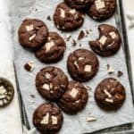 An array of chocolate chip mint cookies on a parchment lined tray with peppermint bark shards around.