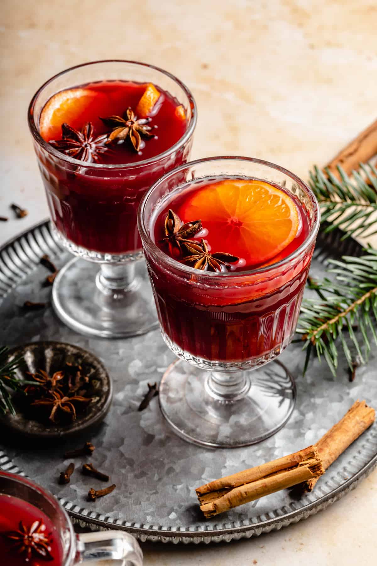 Two glasses of non alcoholic mulled wine with a slice of clementine and star anise on a tray in a Christmas scene.