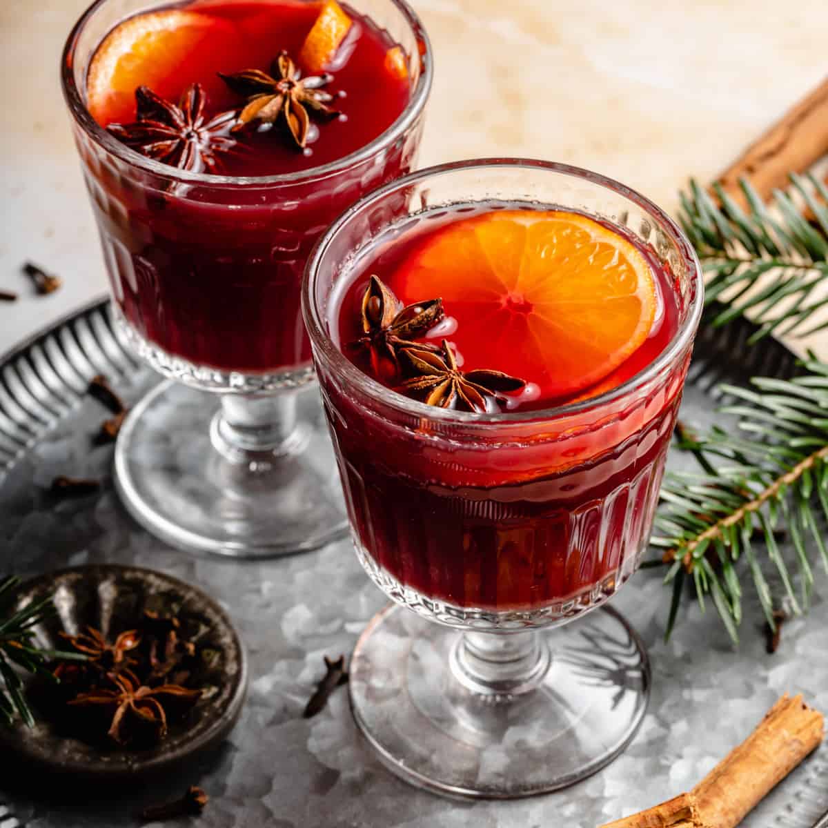 Non alcoholic mulled wine in glasses on a tin tray with spices and slices of clementine.