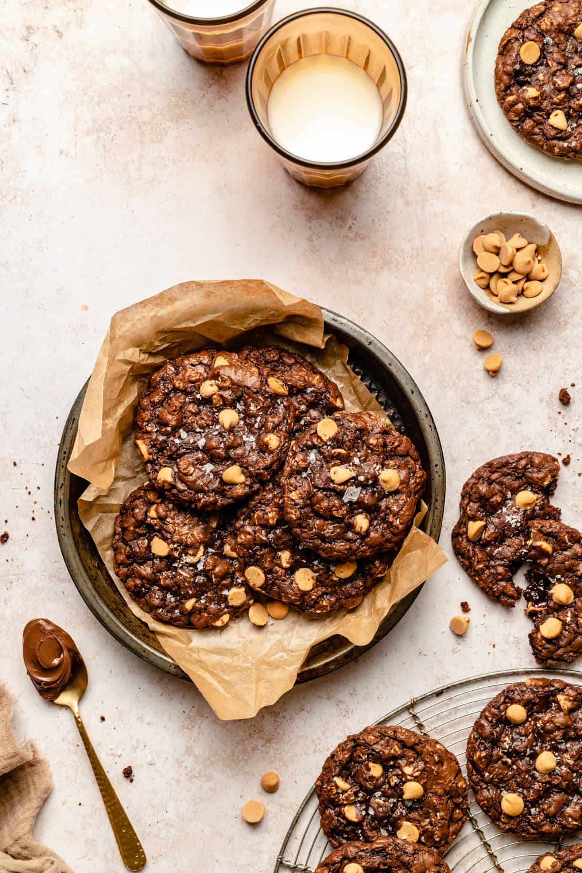 Nutella oatmeal peanut butter chip cookies in a baking tin lined with parchment paper with a broken cookie to the side with a glass of milk.