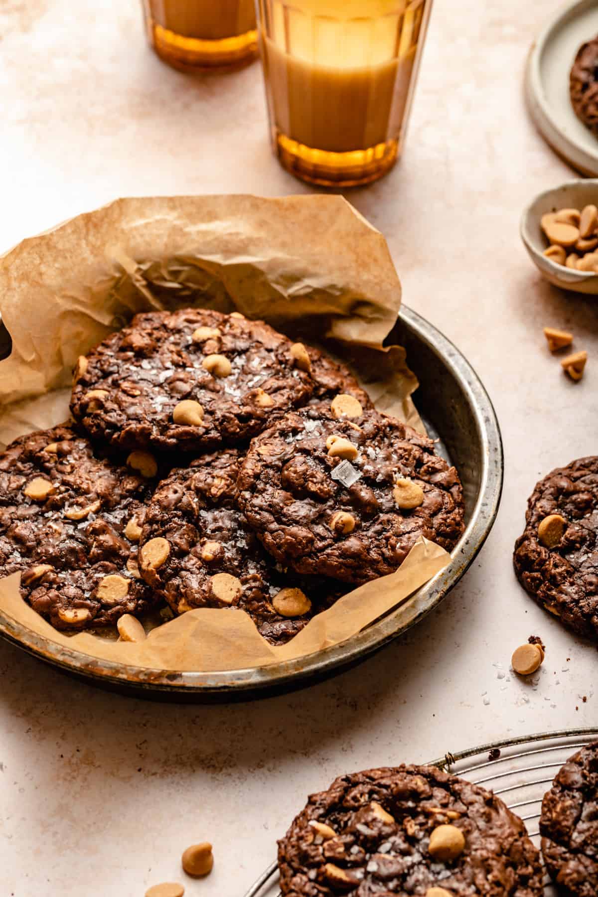 Cookies in a baking tin with parchment a glass of milk and peanut butter chips to the side.