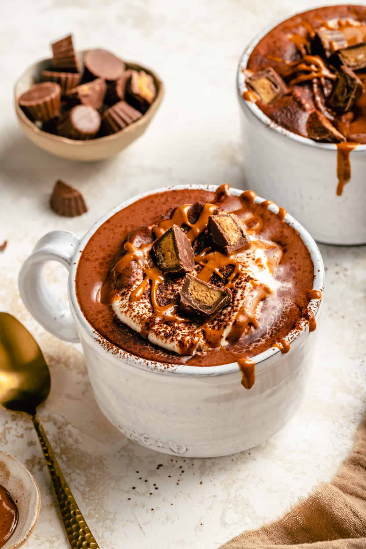 Peanut butter hot chocolate with toppings and a bowl of peanut butter cups behind.
