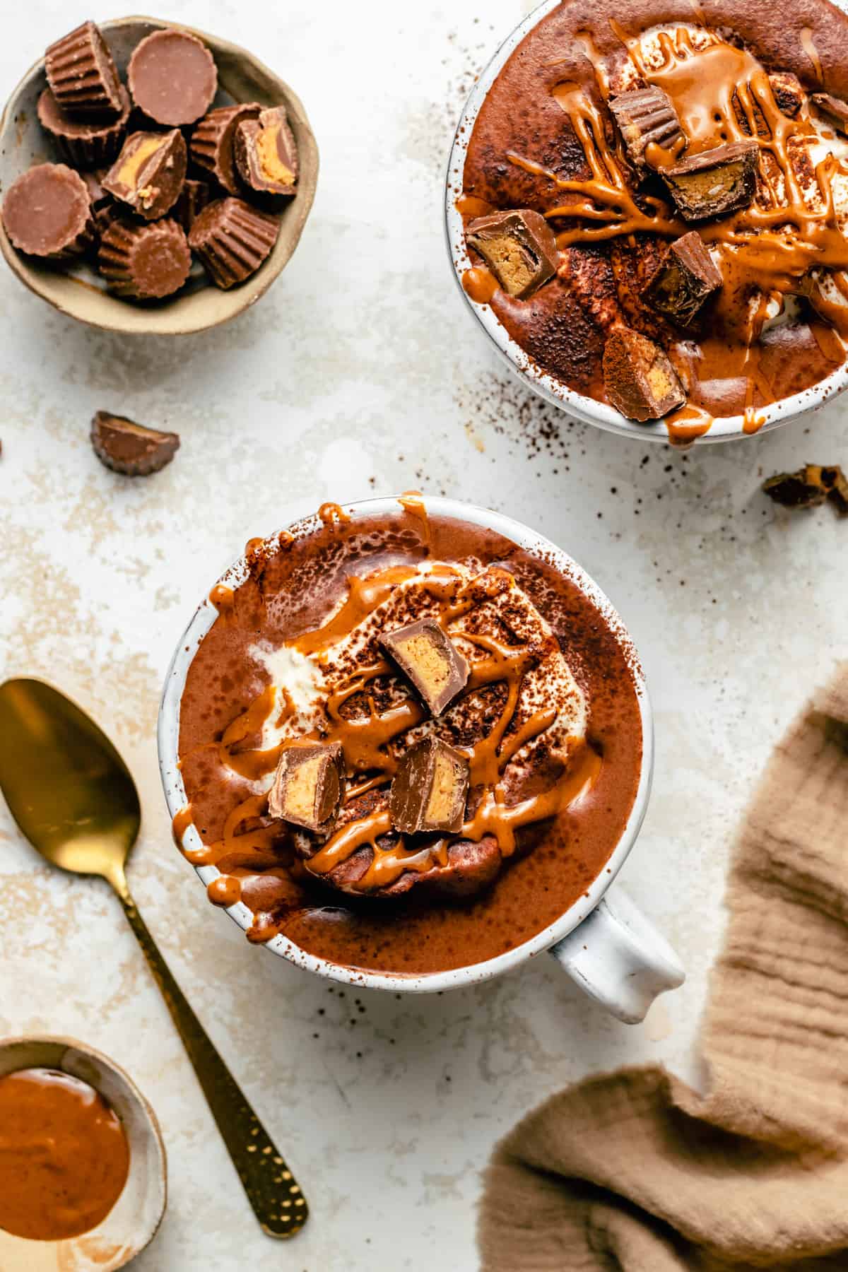 Peanut butter hot chocolate topped with whipped cream, cocoa powder, peanut butter and peanut butter chocolate chips and spoon.