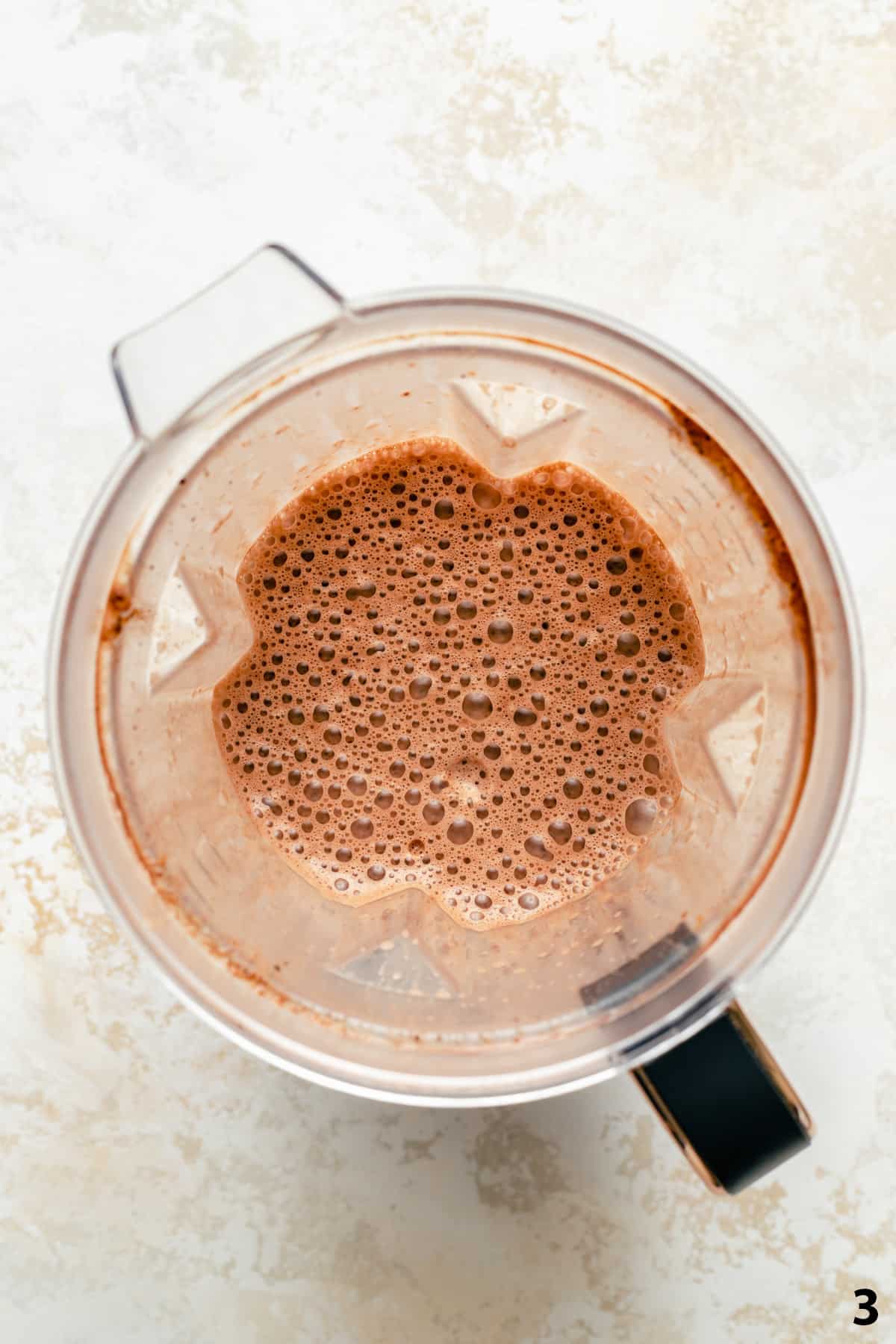 A blender jug with foamy peanut butter hot chocolate blended together.