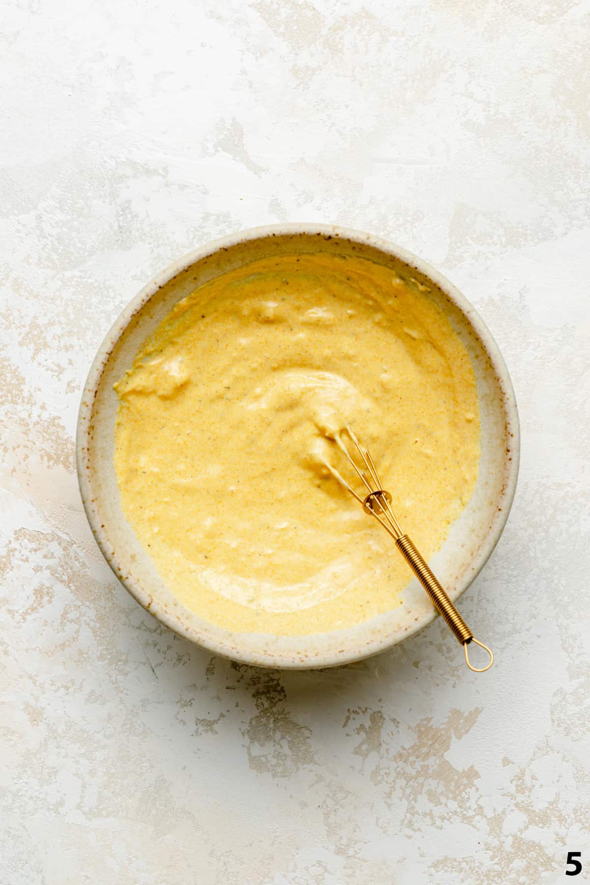 A bowl of the roasted garlic turmeric tahini yoghurt dressing with a small whisk.