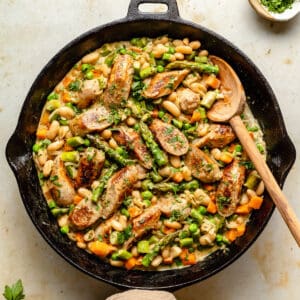 Creamy Chicken Sausage Skillet Recipe in a skillet with a spoon and a napkin around the handle.