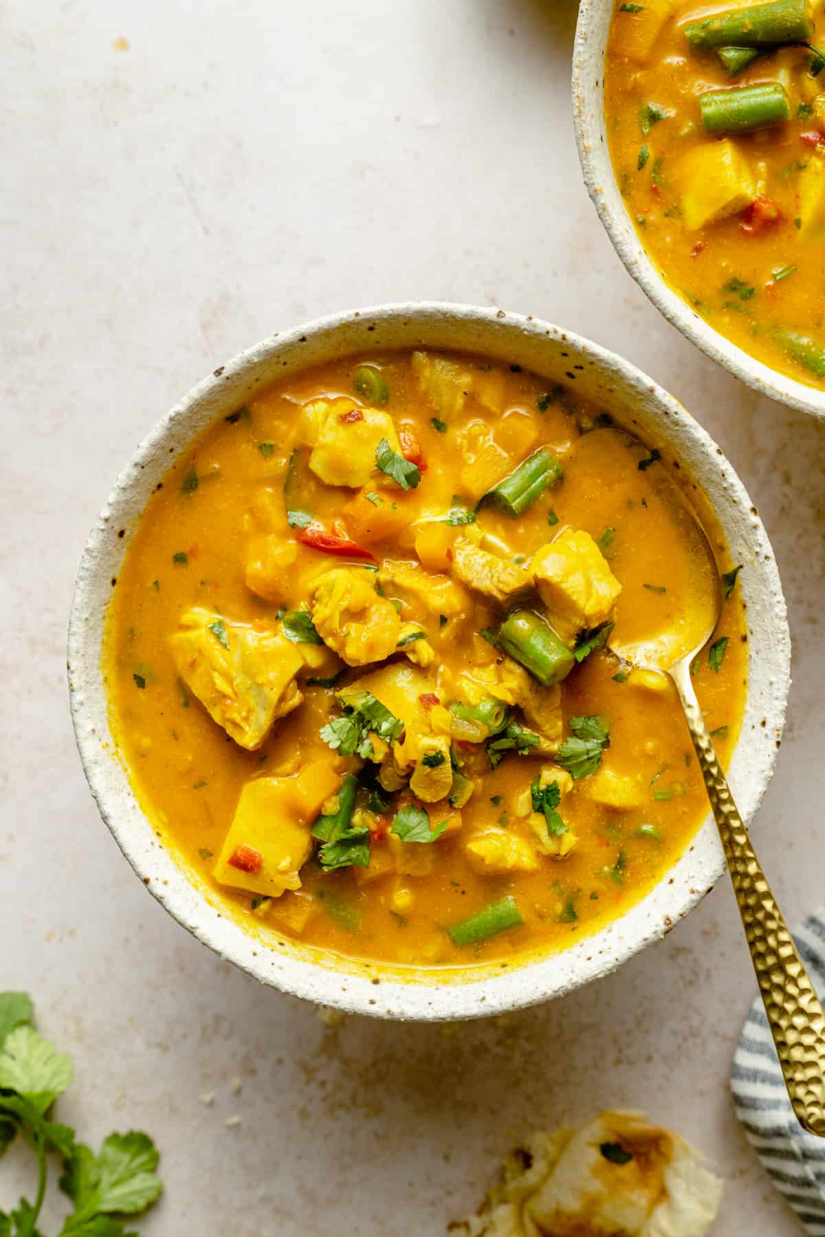 A bowl of coconut curry chicken soup with a gold spoon and some chopped cilantro on top.