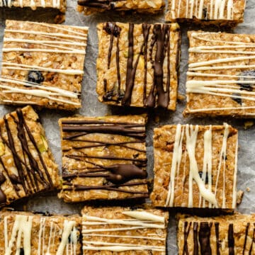 An array of no bake granola bars on parchment paper with chocolate drizzled over the top.