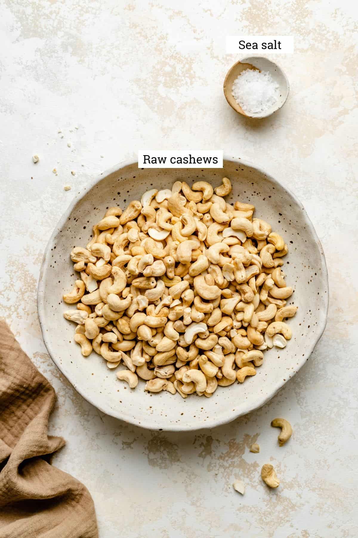 A bowl of raw cashew nuts and a smaller dish of flaky sea salt.