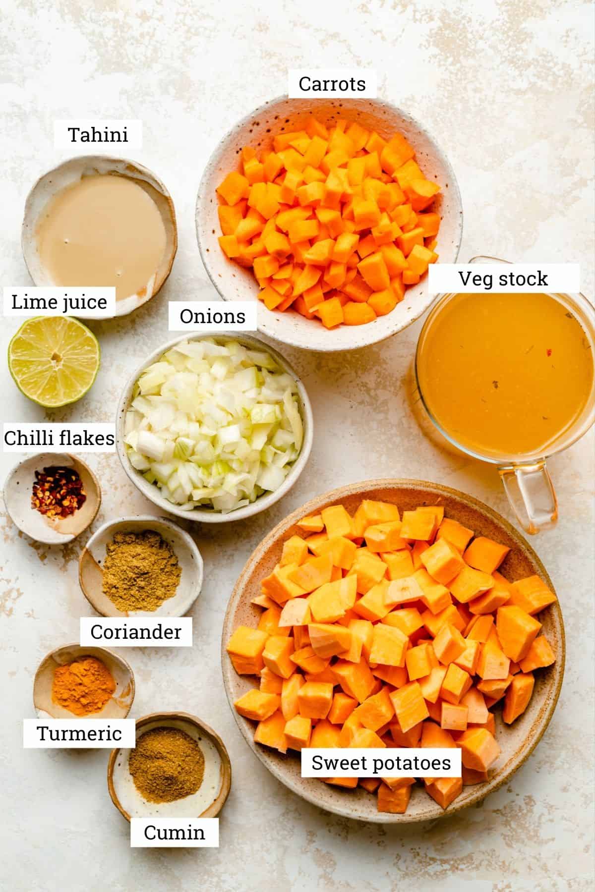 Ingredients for spiced sweet potato and carrot soup in various bowls including spices and vegetable stock.