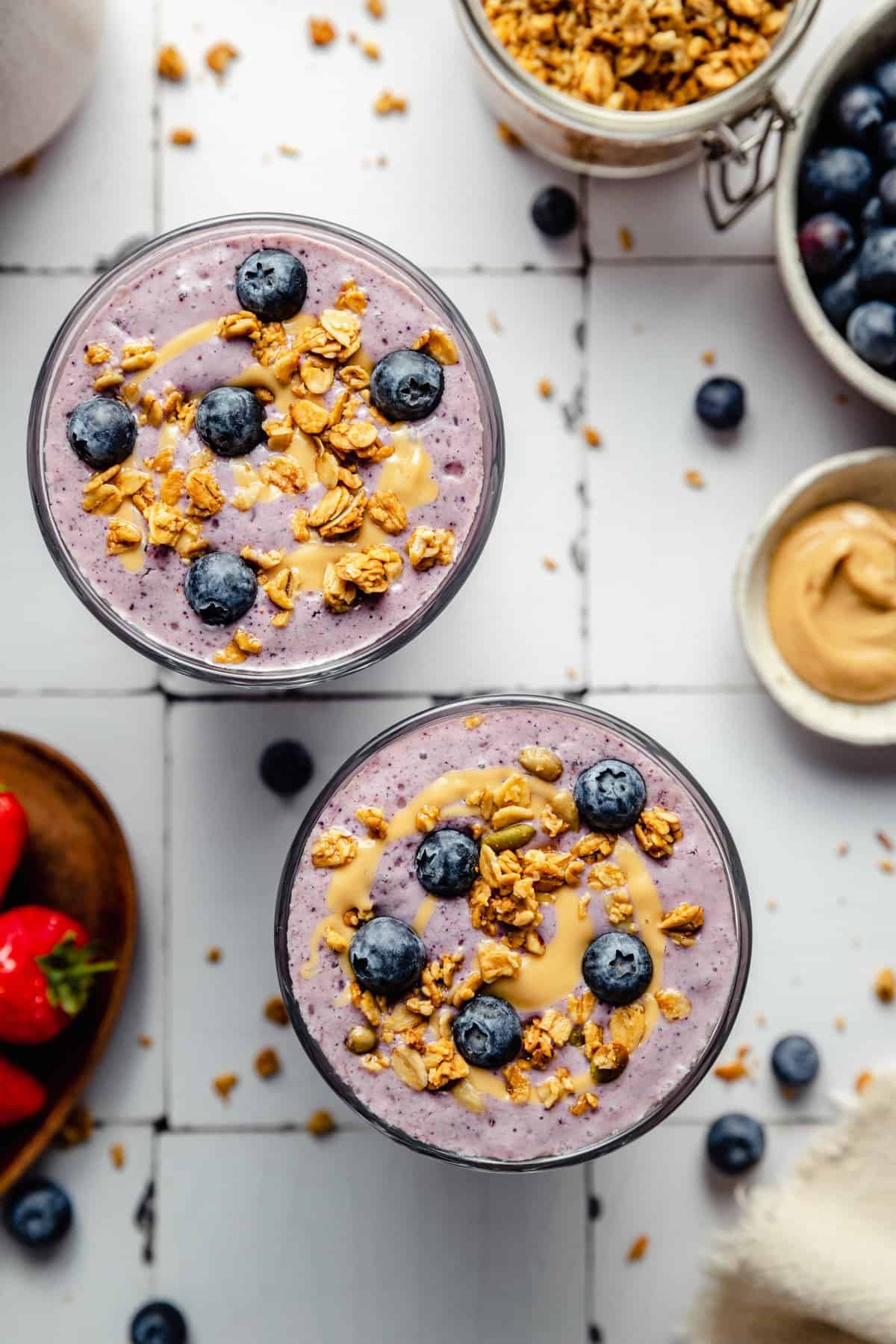 Strawberry blueberry smoothie served in glasses topped with cashew butter, blueberries and granola.
