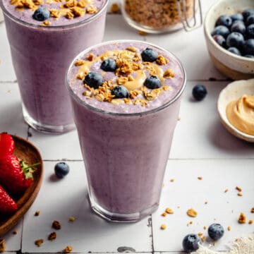 Strawberry blueberry smoothie in glasses with blueberries, cashew butter and granola.