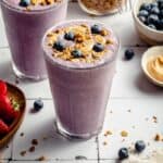 Strawberry blueberry smoothie in two glasses with granola, blueberries and cashew butter on top.