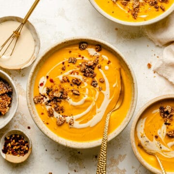 Sweet potato and carrot soup in bowls with spoons and a drizzle of tahini on top.