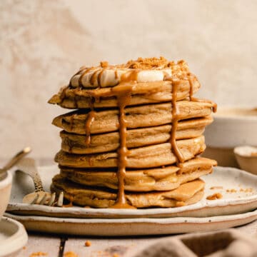 A stack of biscoff pancakes on a plate with biscoff cream on top and drips of biscoff pouring down the sides.
