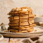 biscoff pancakes in a stack on a plate with drips of biscoff pouring down the sides.
