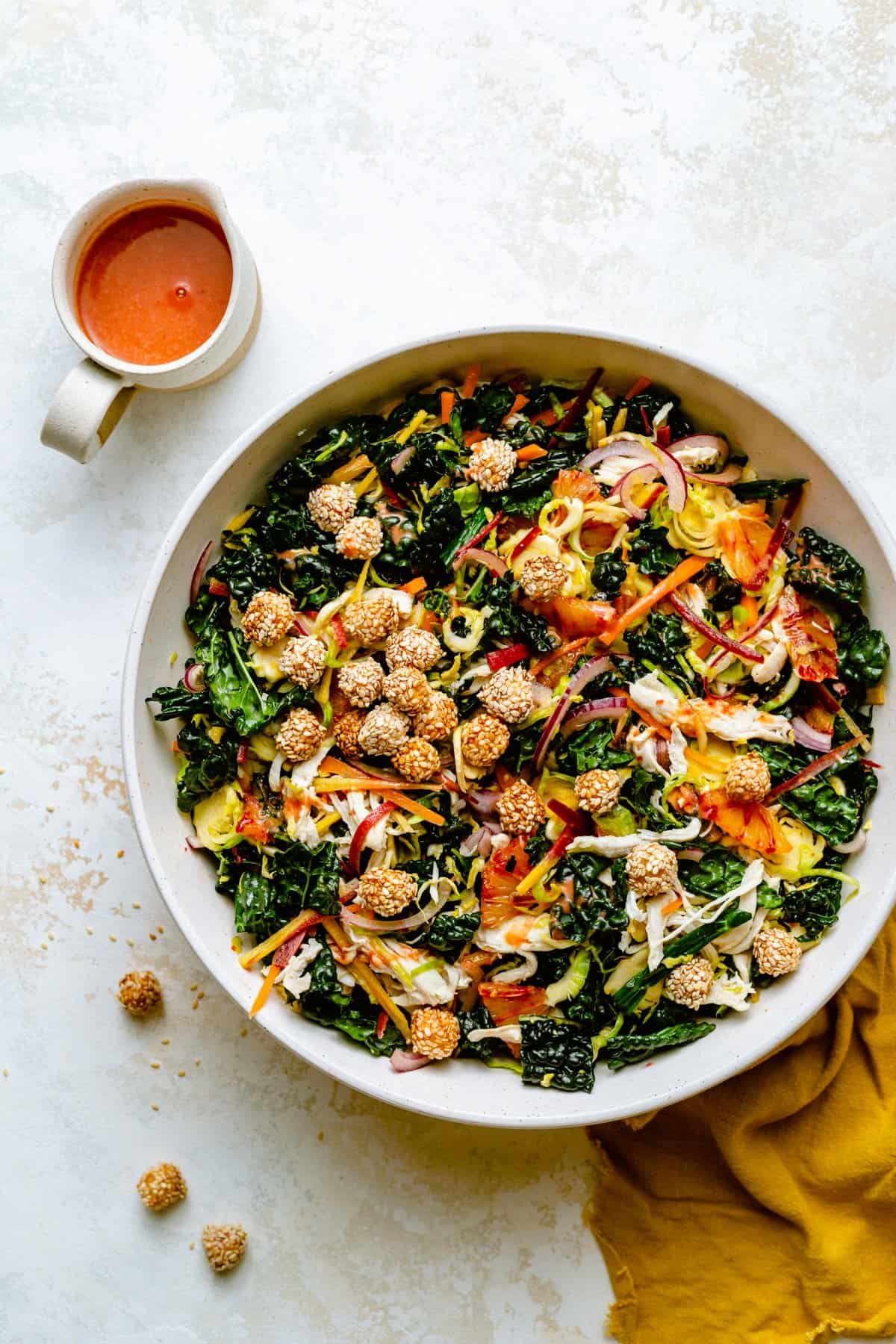 Kale citrus salad assembled and dressed in a serving bowl with crispy sesame chickpeas on top with a jug of dressing nearby.