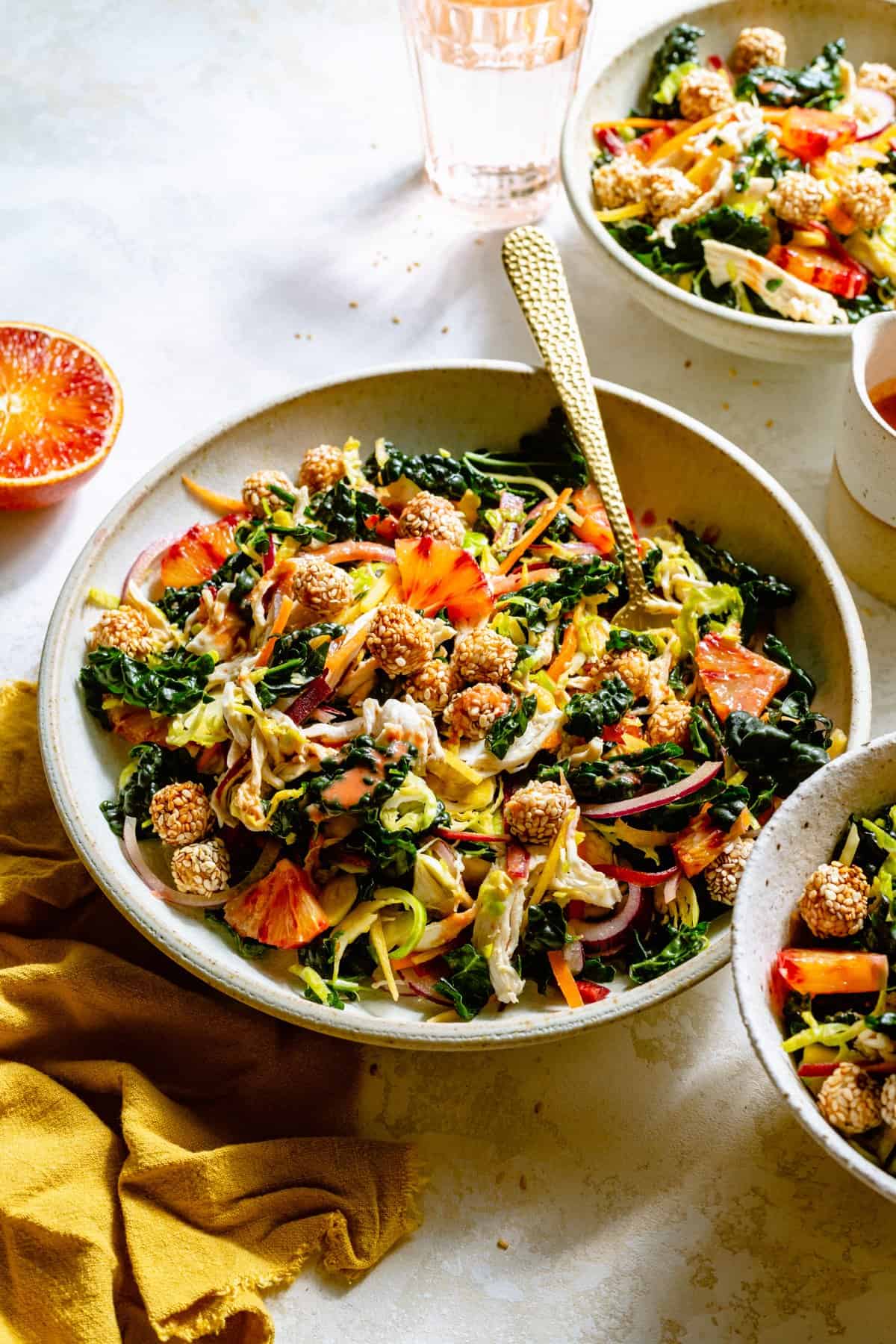 Various bowls of kale citrus salad dressed with a fork and crispy chickpeas around.