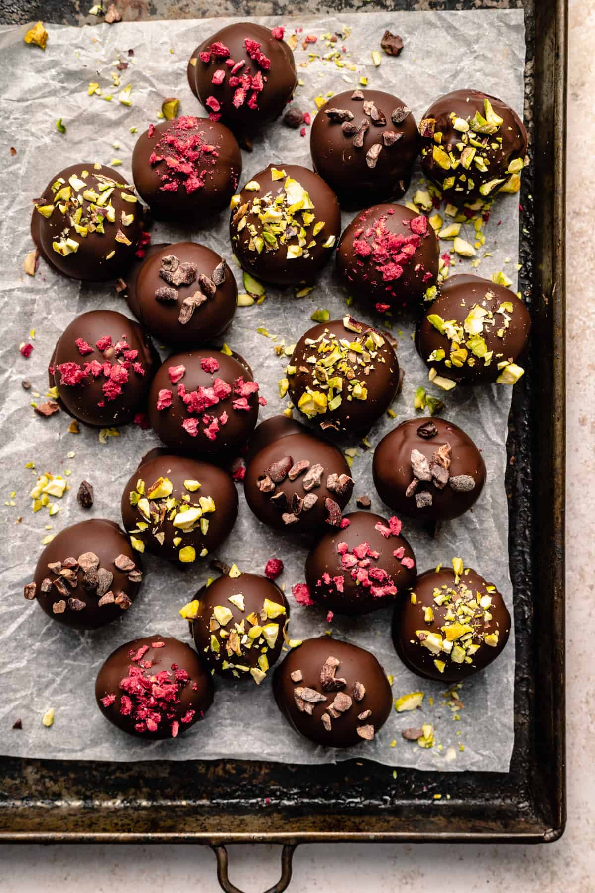 A tray of raspberry dark chocolate truffles with toppings of pistachios, freeze dried raspberries and cacao nibs.