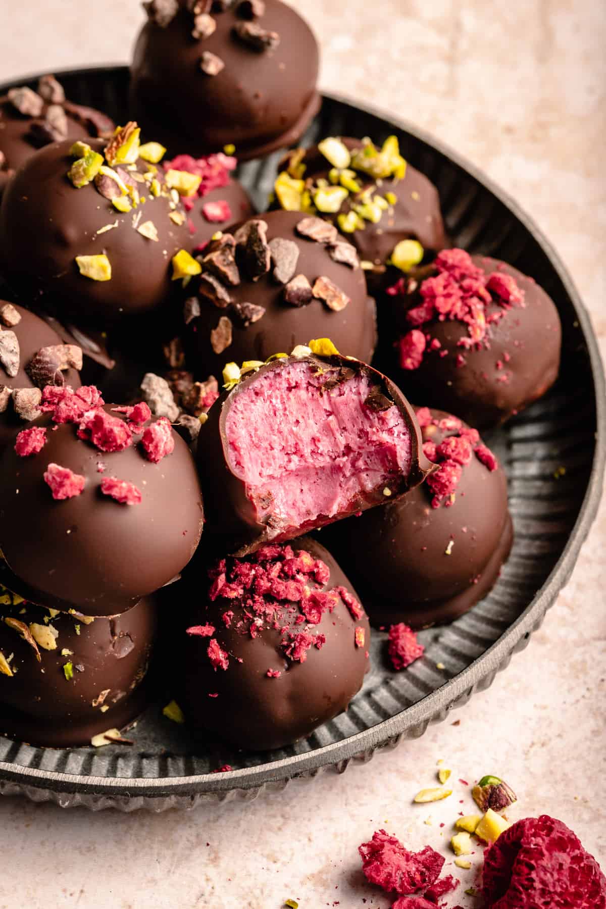 a plate with raspberry dark chocolate truffles on topped with various toppings and one with a bite taken out of it. 