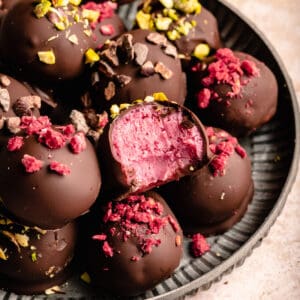 Raspberry Dark Chocolate Truffles on a plate, one on top with a bite showing the vivid raspberry centre.