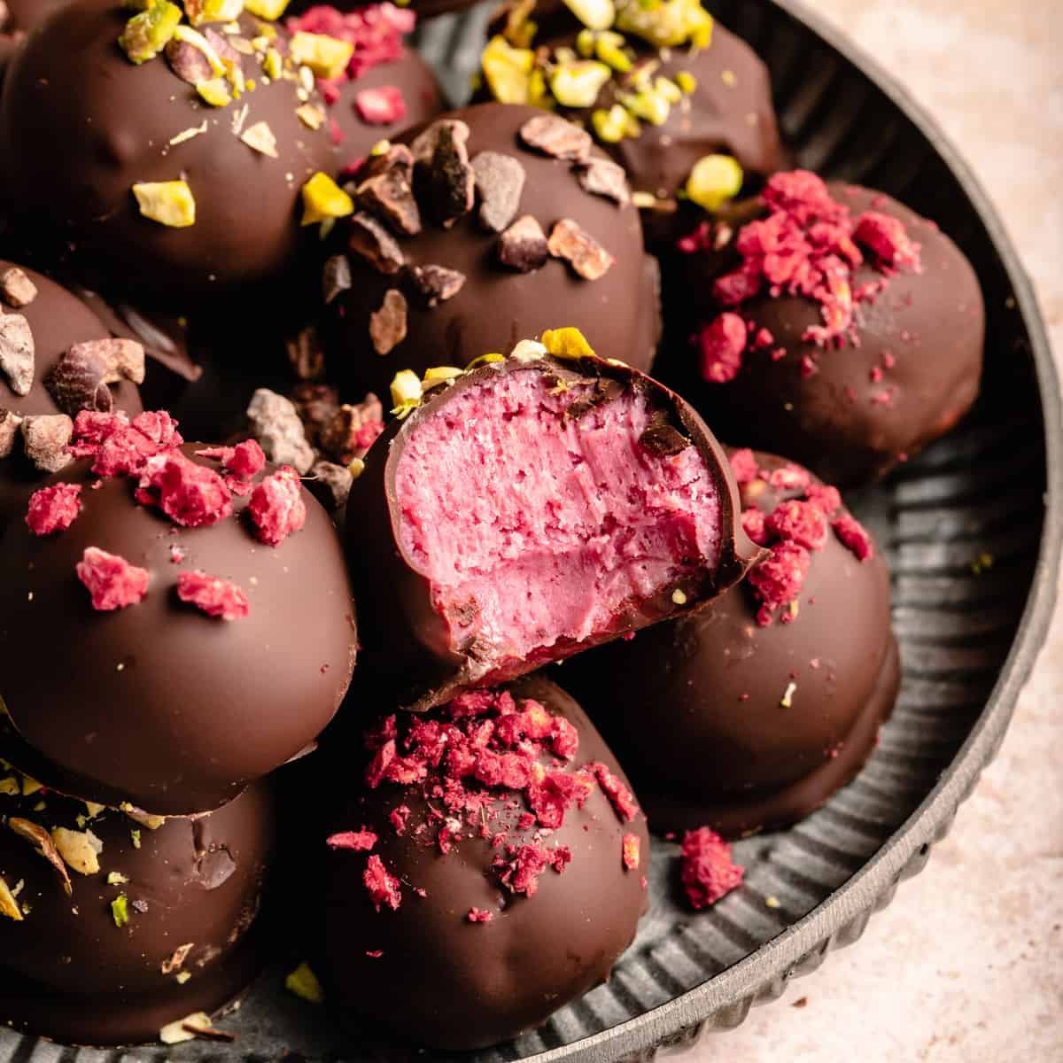 A plate of raspberry truffles with one on top with a bite taken out showing the pink center.