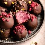 Raspberry dark chocolate truffles on a plate with one with a bite taken out of.