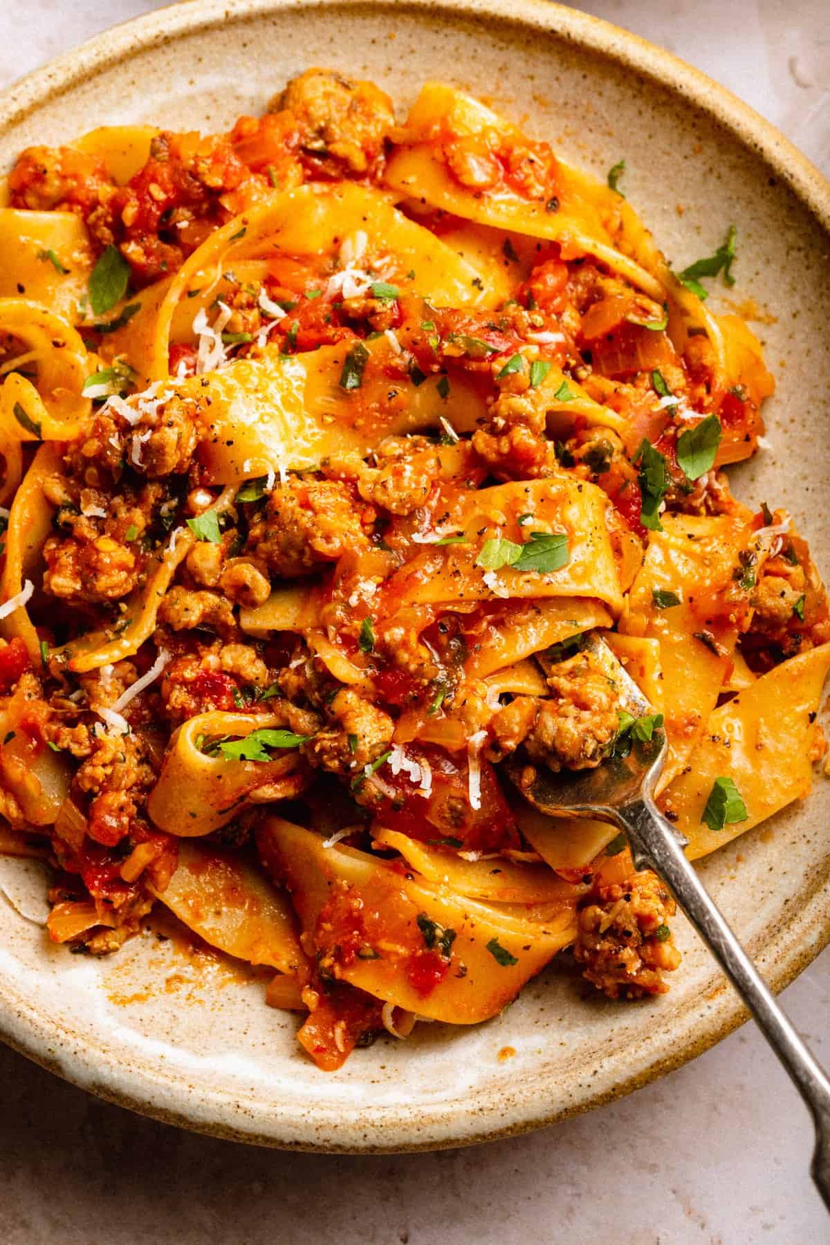 Close up of sausage ragu with pappardelle in a bowl with the pasta wrapped around a fork and parmesan shavings on top.