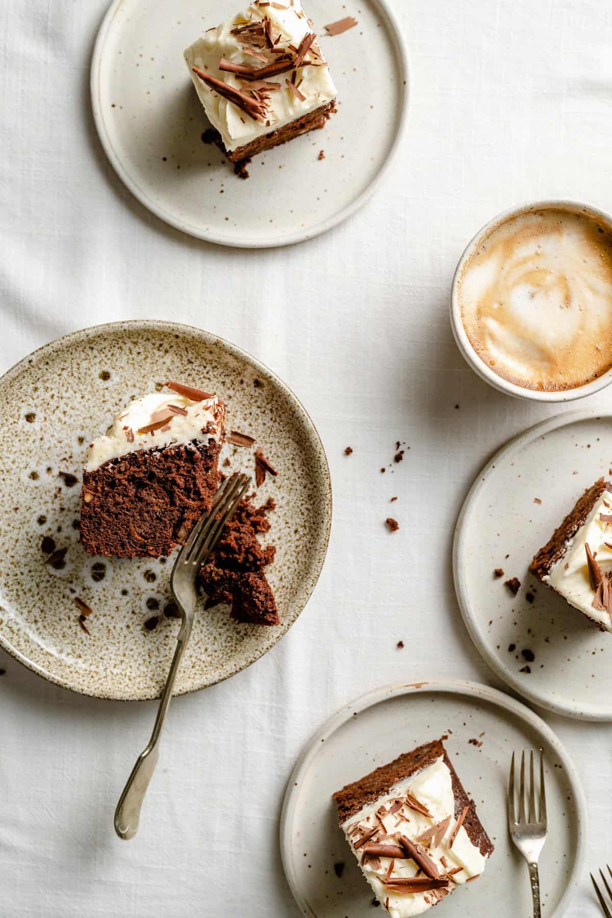 Multiple plates with slices of cake on with a coffee, one cake being cut into with a fork. 