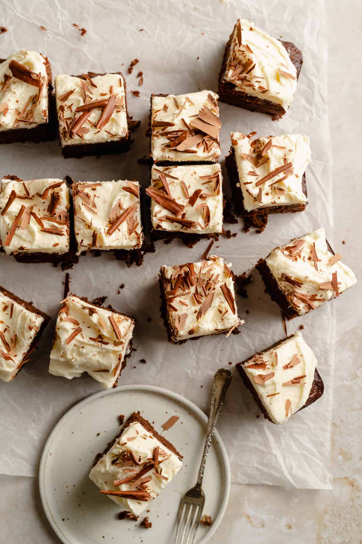 An array of carrot cake squares with chocolate shavings on top of parchment paper.