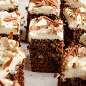 Chocolate carrot cake sliced into squares with white chocolate cream cheese frosting on top and chocolate shavings.