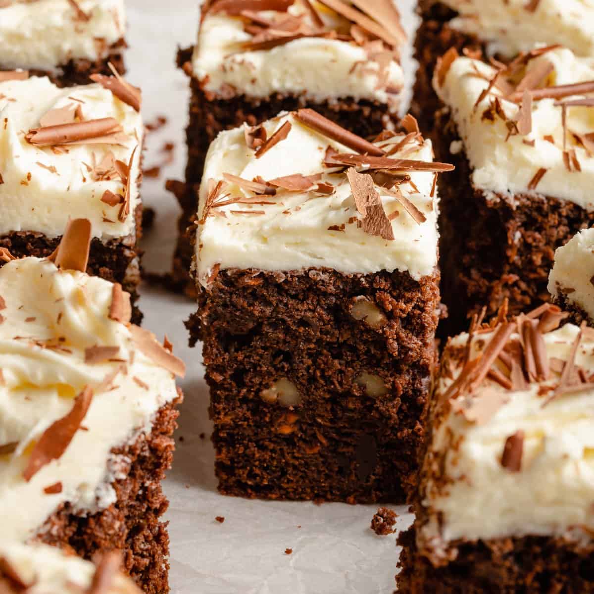 Chocolate carrot cake cut up into squares with white chocolate cream cheese frosting on top.