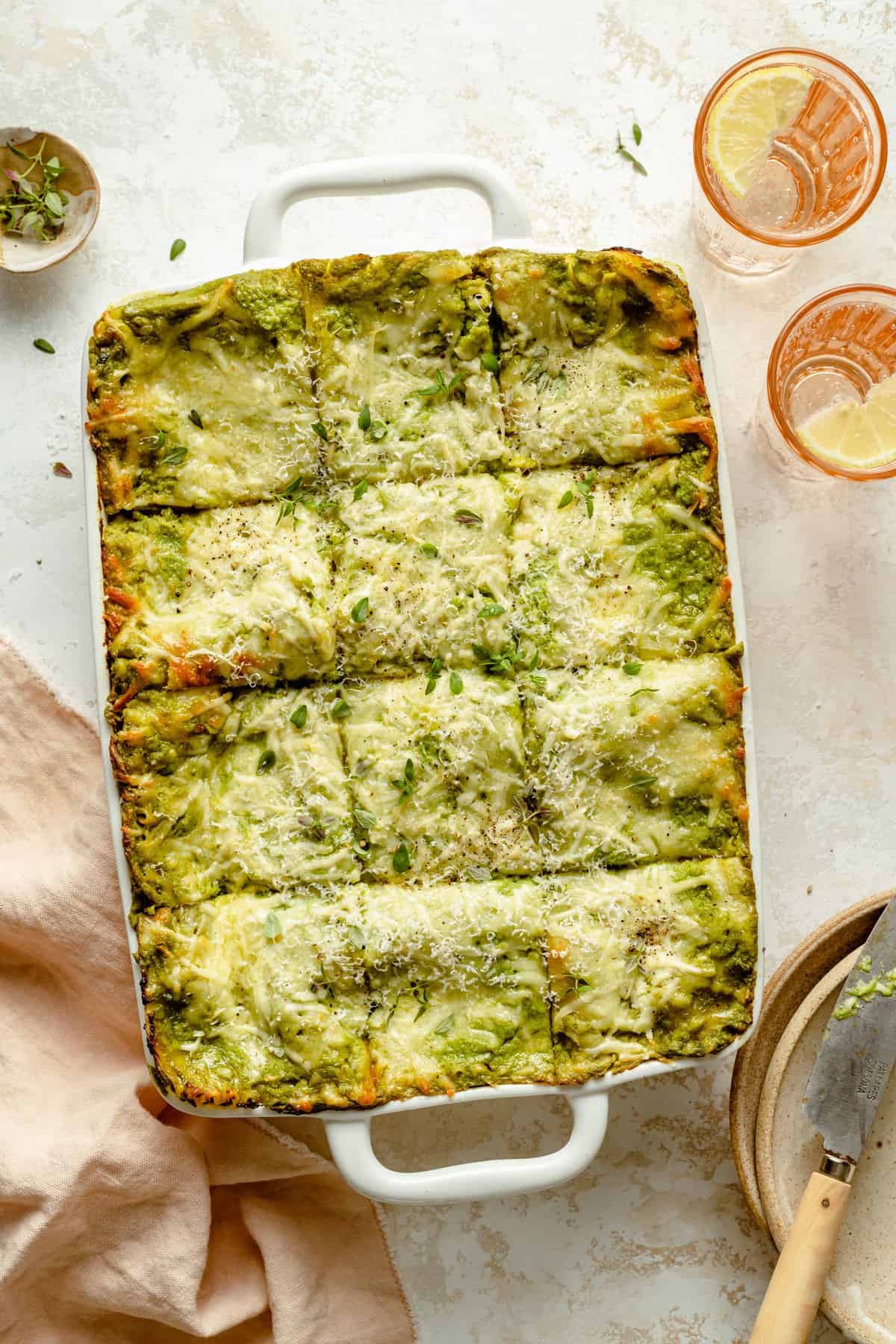 A cheesy topped chicken lasagna cut into 12 portions in a 9x13 baking dish with a knife to the side.