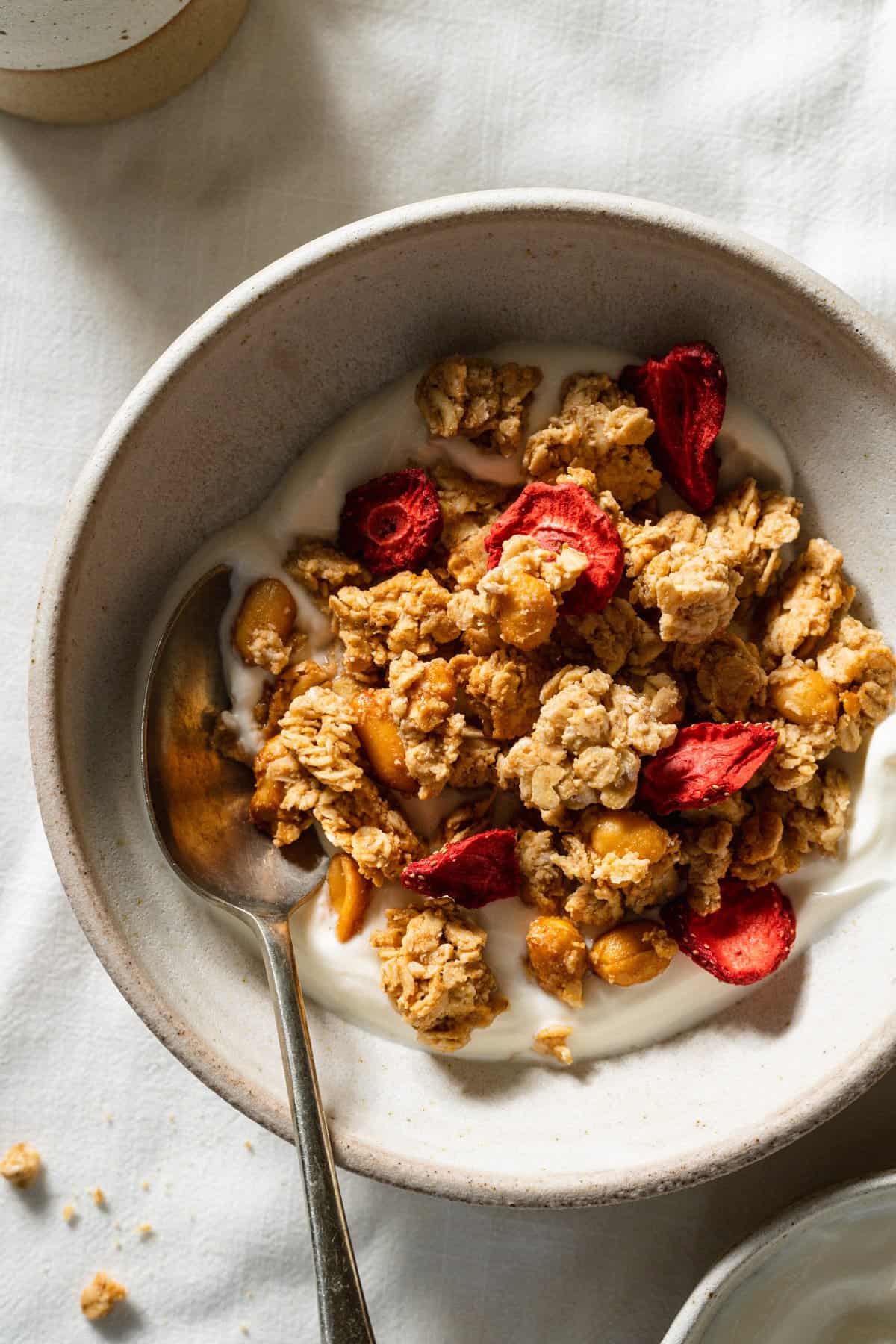 A bowl of granola served on top of yoghurt with a spoon.