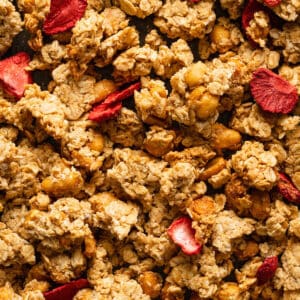 Peanut butter granola on a baking sheet studded with honey roasted peanuts and dried strawberries.
