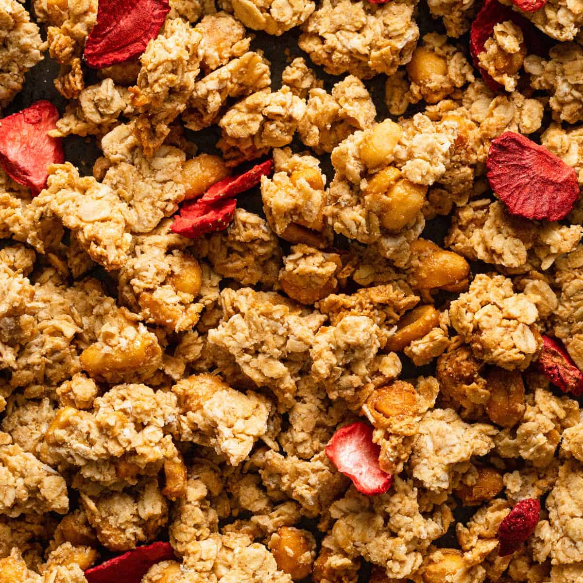 A baking sheet of peanut butter granola showing the peanuts and freeze dried strawberries.