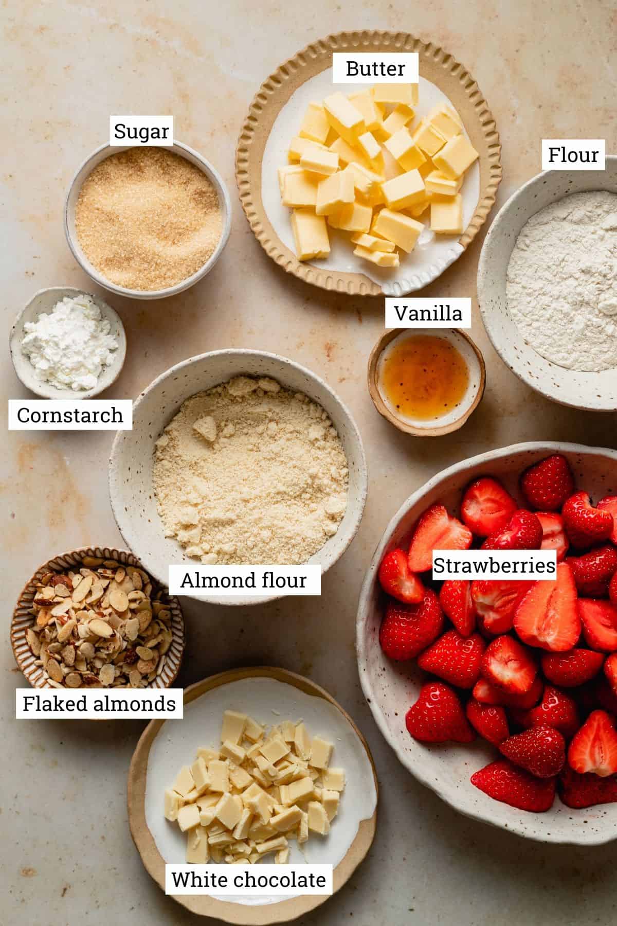 Ingredients for the crumble in various bowls including strawberries, sugar, butter and flour.