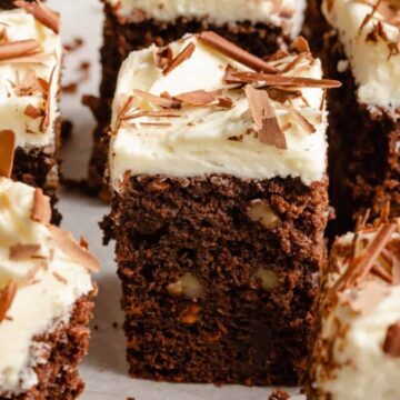 Chocolate carrot cake cut up into squares decorated with cream cheese frosting and chocolate shavings.