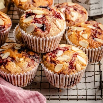 Cherry sourdough muffins stacked on a wire cooling rack with a pink napkin in the foreground.