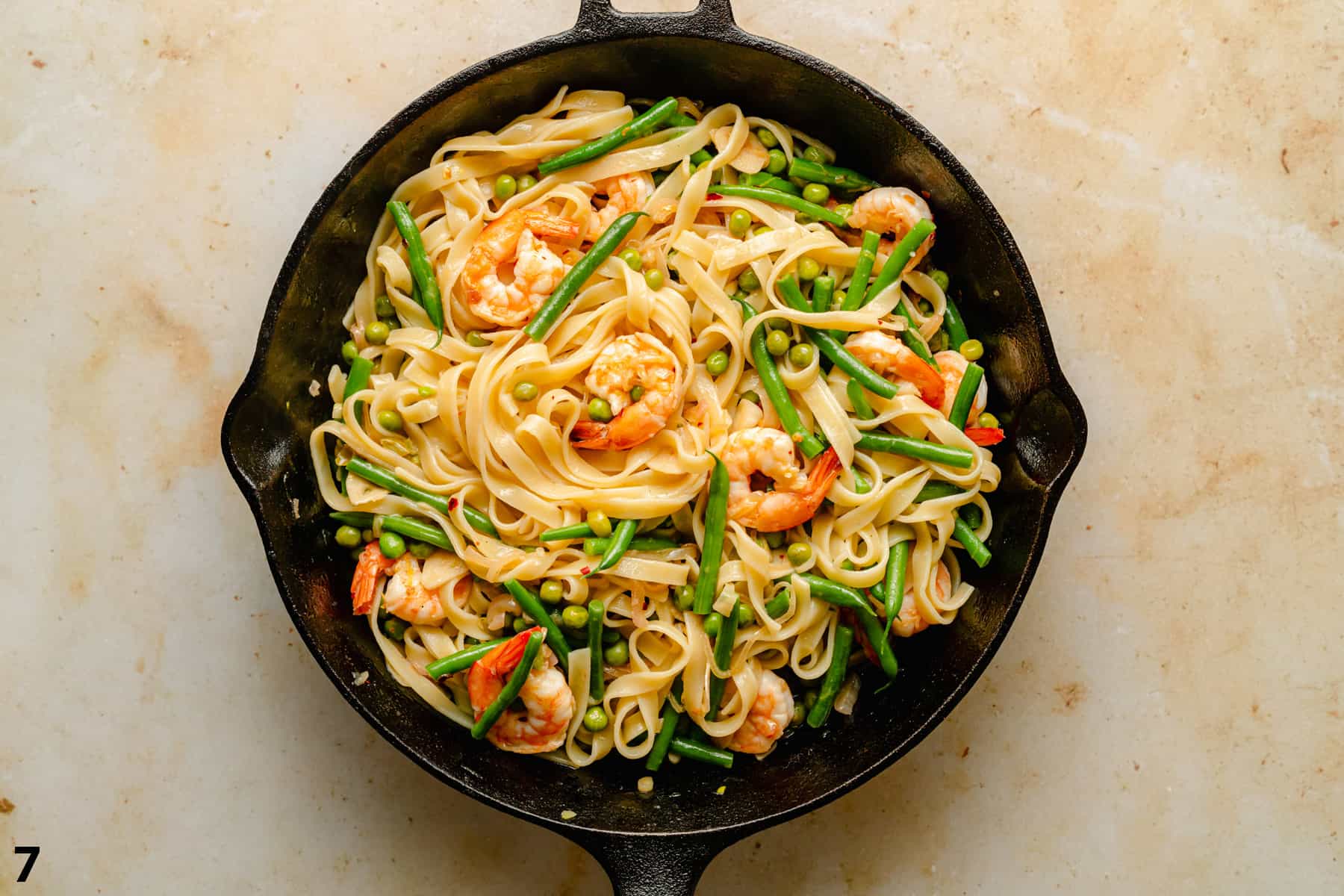 Lemon garlic shrimp pasta finished in a cast iron skillet on a warm background.