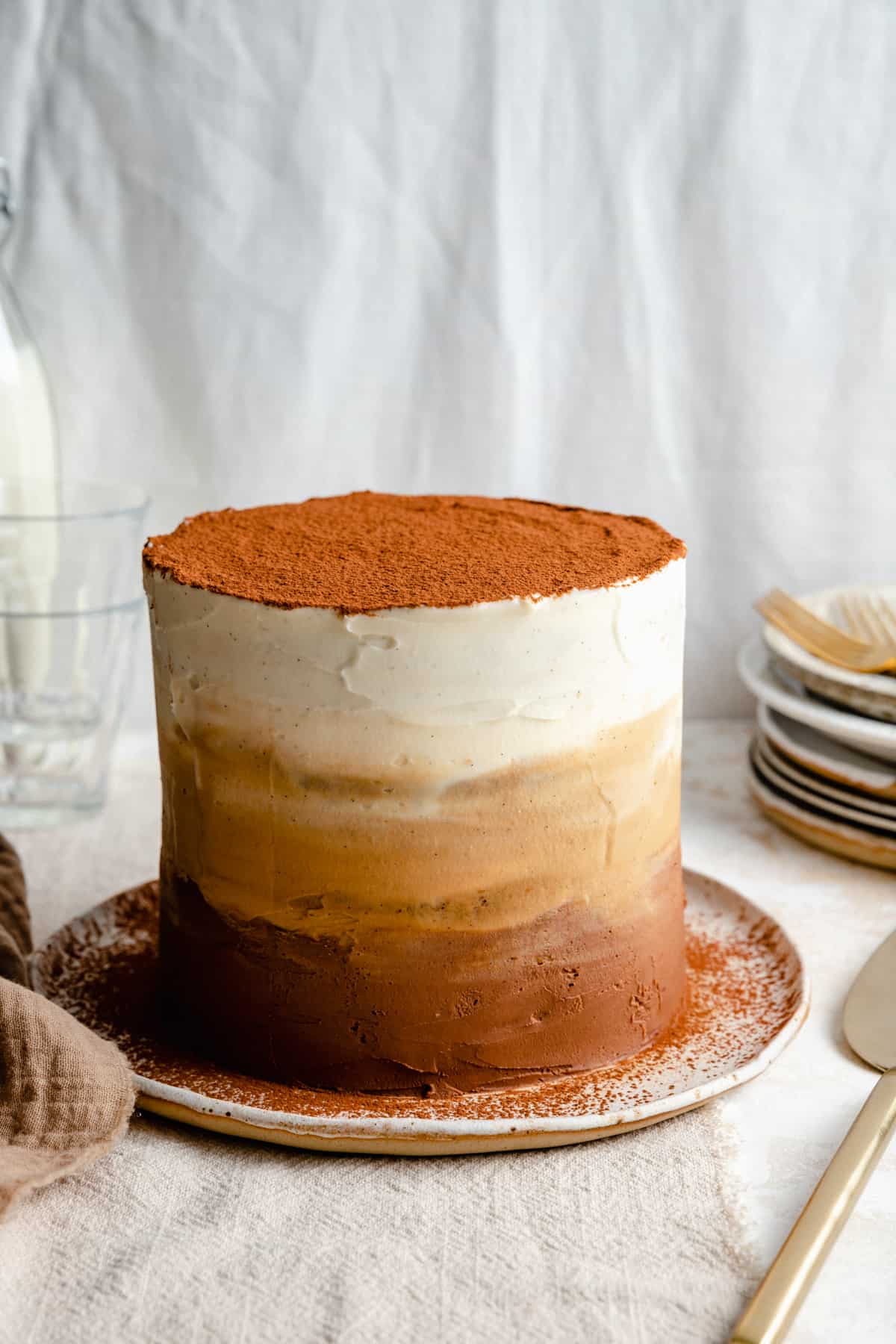 Tiramisu cake with ombre mascarpone frosting dusted with cocoa powder on a plate.